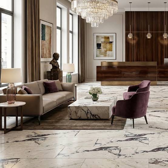 A luxurious modern living room featuring continuous Calacatta Viola marble tile flooring, a deep-veined marble coffee table, contemporary low-slung seating with warm velvet accents, and refined wood paneling under an elegant crystal chandelier.